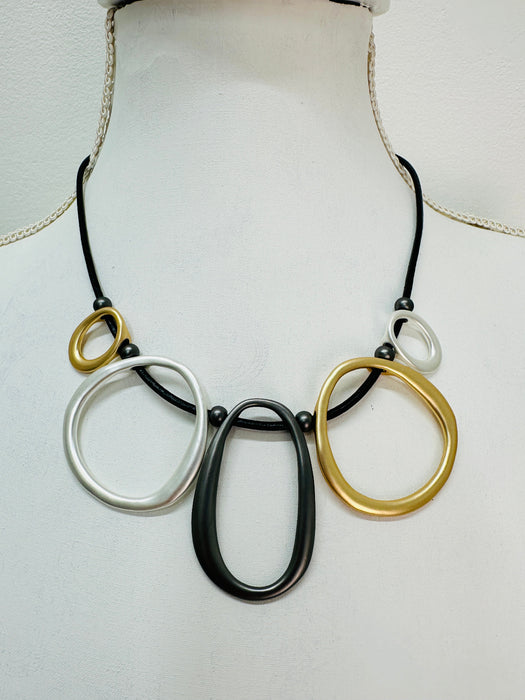 close-up of black faux leather necklace with mixed-metal oval links in gold, silver and dark grey tones.