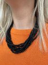 A person wearing a black multistrand beaded necklace with a large loop and button fastening.