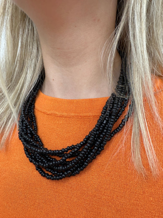 A person wearing a black multistrand beaded necklace with a large loop and button fastening.