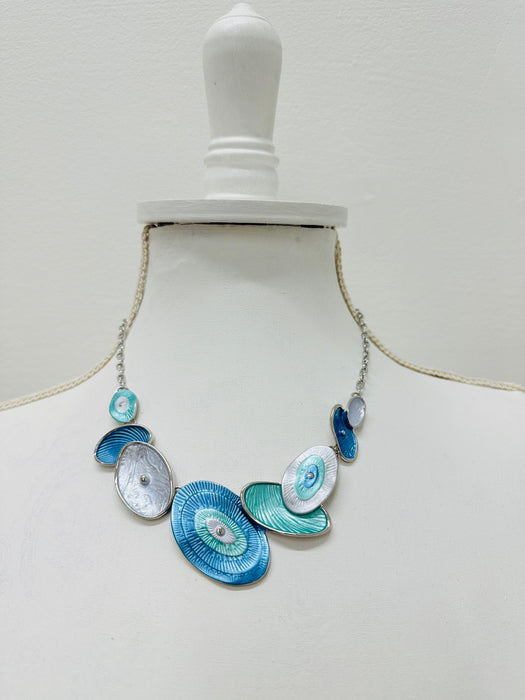 Blue and aqua enamel geometric statement necklace with silver tone chain and textured oval accents displayed on a mannequin.