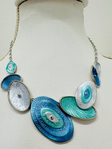 Blue and aqua enamel geometric statement necklace with silver tone chain and textured oval accents displayed on a mannequin.