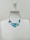 Blue and aqua enamel geometric statement necklace with silver tone chain and textured oval accents displayed on a mannequin.