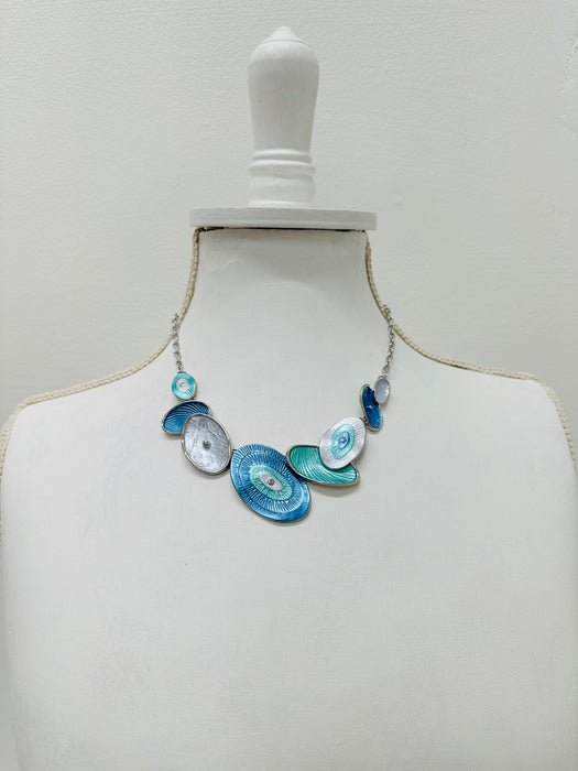 Blue and aqua enamel geometric statement necklace with silver tone chain and textured oval accents displayed on a mannequin.