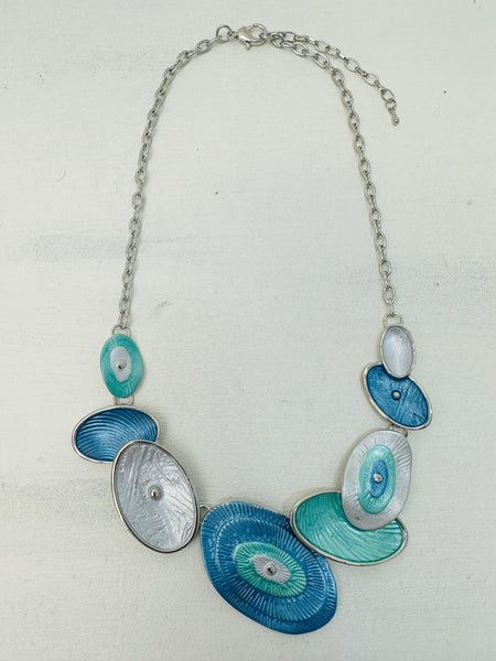 Blue and aqua enamel geometric statement necklace with silver tone chain and textured oval accents displayed on a white background.