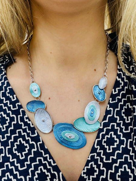 Blue and aqua enamel geometric statement necklace with silver tone chain and textured oval accents displayed on a model.