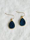 Teardrop-shaped earrings with blue druzy stones on gold hooks against a white background