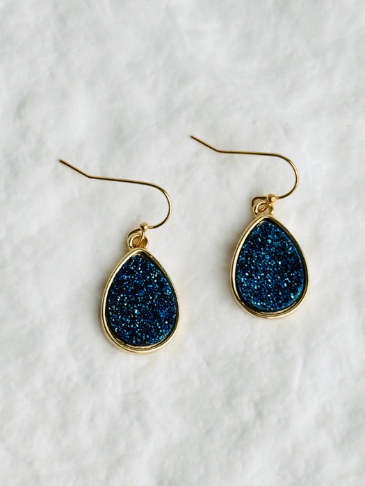 Teardrop-shaped earrings with blue druzy stones on gold hooks against a white background
