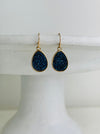 Teardrop-shaped earrings with blue druzy stones on a white pedestal