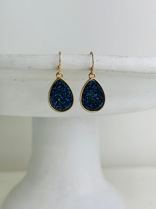 Teardrop-shaped earrings with blue druzy stones on a white pedestal
