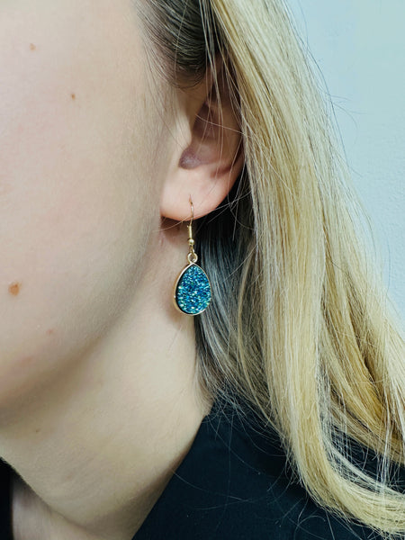 Close-up of a person wearing a blue druzy earring with gold setting.
