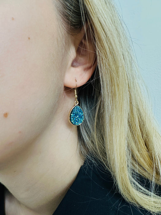Close-up of a person wearing a blue druzy earring with gold setting.