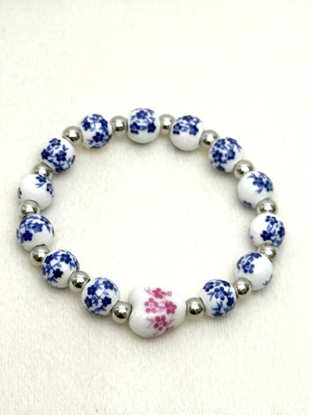 Blue and white porcelain bead stretch bracelet with pink floral centre bead and silver spacers on a white background
