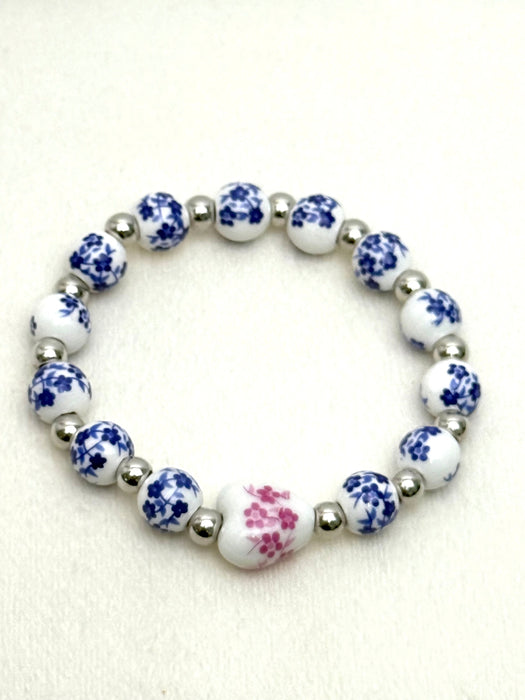 Blue and white porcelain bead stretch bracelet with pink floral centre bead and silver spacers on a white background