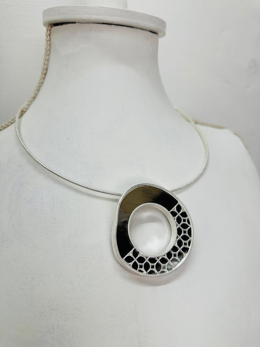 close-up of modern silver tone necklace with a round pendant in sleek dark brown and silver, finished with
delicate cut out details
