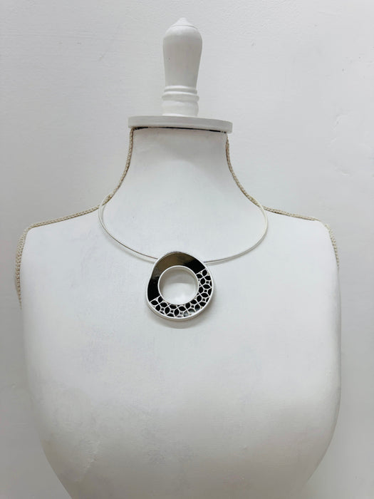 modern silver tone necklace with a round pendant in sleek dark brown and silver, finished with
delicate cut out details displayd on a mannequin