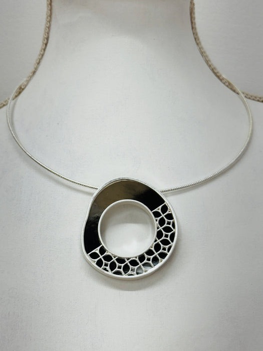 close-up of modern silver tone necklace with a round pendant in sleek dark brown and silver, finished with
delicate cut out details