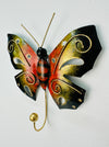 A handmade and hand painted metal butterfly hook in orange with gold detailing, mounted on a wall.