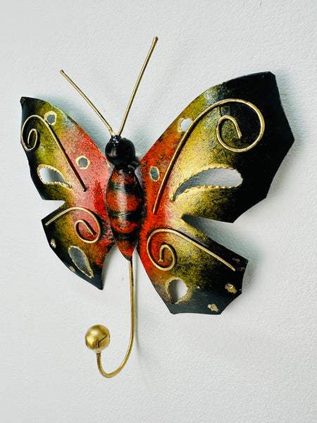 A handmade and hand painted metal butterfly hook in orange with gold detailing, mounted on a wall.