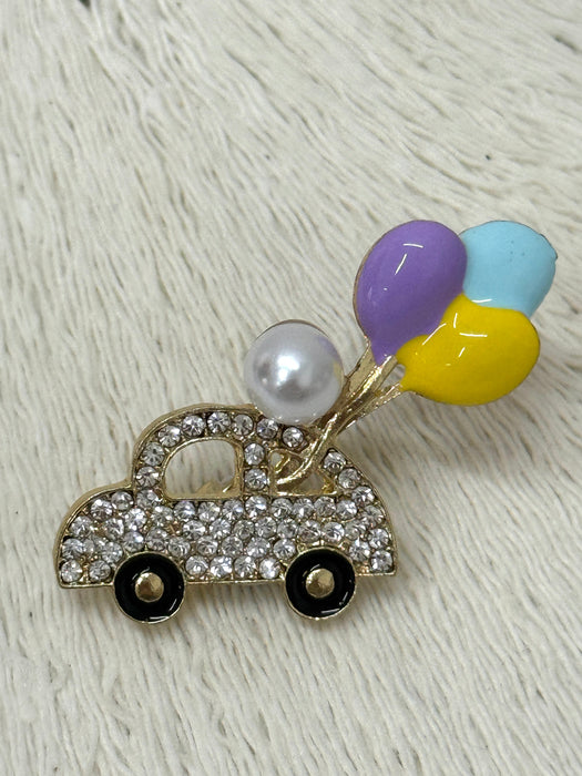 A gold-toned brooch in the shape of a car decorated with multicolored balloons and pearls.