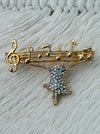 Gold-tone brooch featuring a crystal cat hanging from musical notes