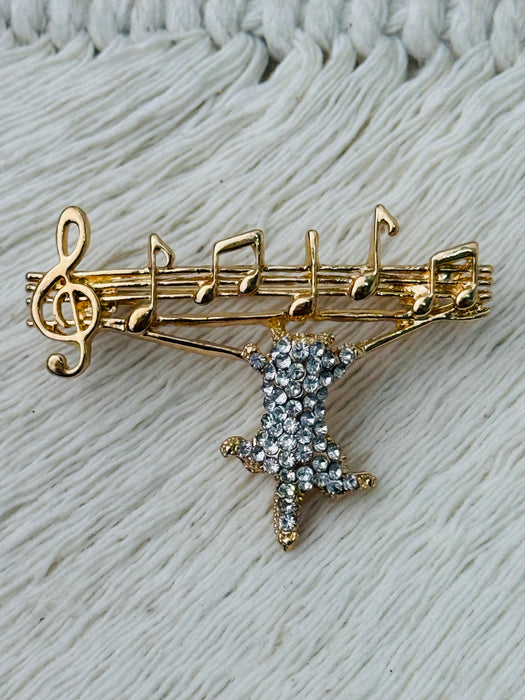 Gold-tone brooch featuring a crystal cat hanging from musical notes