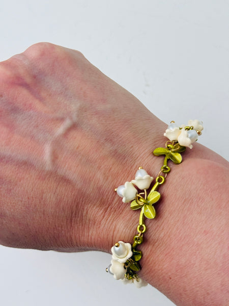 Gold-tone adjustable charm bracelet with white lily of the valley pearl-effect drops and green enamel leaves displayed on a model.