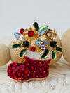 Decorative brooch with red boot, green leaves, and multicolored stones on a white background