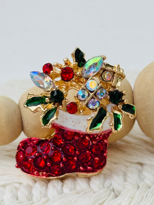 Decorative brooch with red boot, green leaves, and multicolored stones on a white background