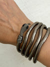 A close-up of a person's wrist wearing a stack of dark metallic snake-themed bracelets, including a prominent snake head clasp and coiled snake bangles.