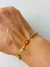 A gold-tone bracelet with colorful floral accents displayed on a person's wrist.