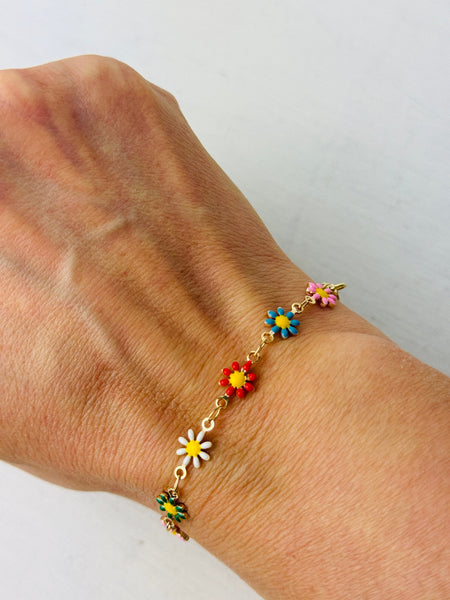 A gold-tone bracelet with colorful floral accents displayed on a person's wrist.