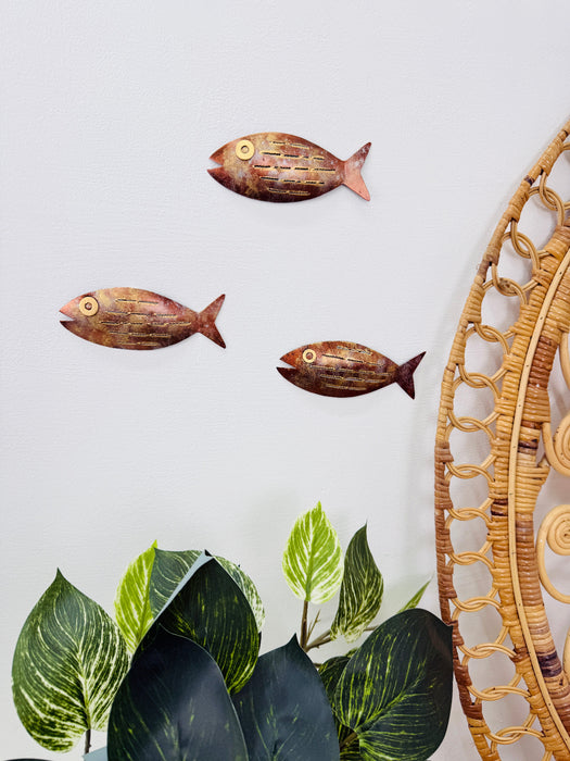 Copper and bronze metal fish wall art displayed with indoor plants on a light wall