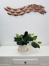 Large copper mottled metal fish shoal wall art displayed above a white cabinet with a plant
