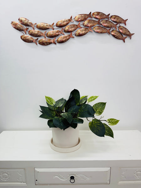Large copper mottled metal fish shoal wall art displayed above a white cabinet with a plant