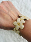 Bracelet with cream floral design and gold accents on a wrist against a white background