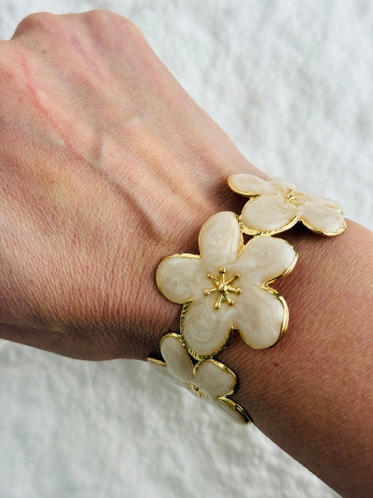 Bracelet with cream floral design and gold accents on a wrist against a white background