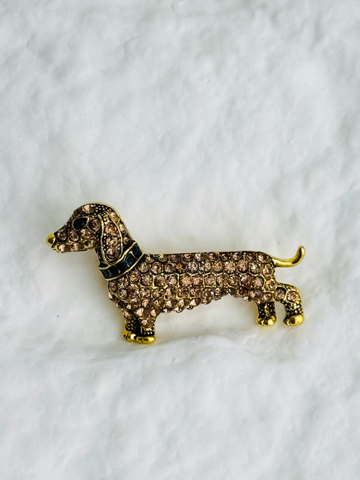 Gold and brown dog-shaped brooch on a white fabric background