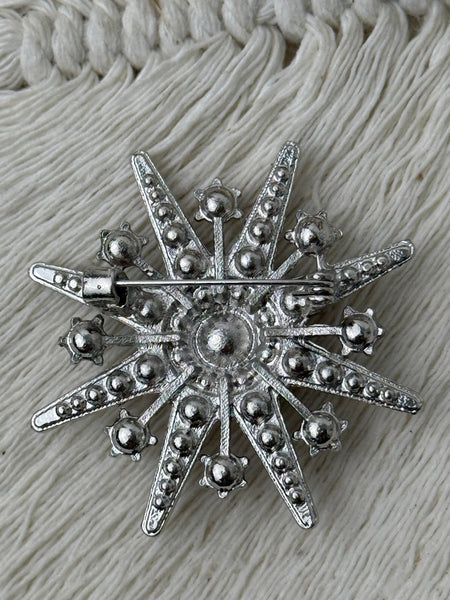back view of silver star-shaped brooch on a textured fabric background