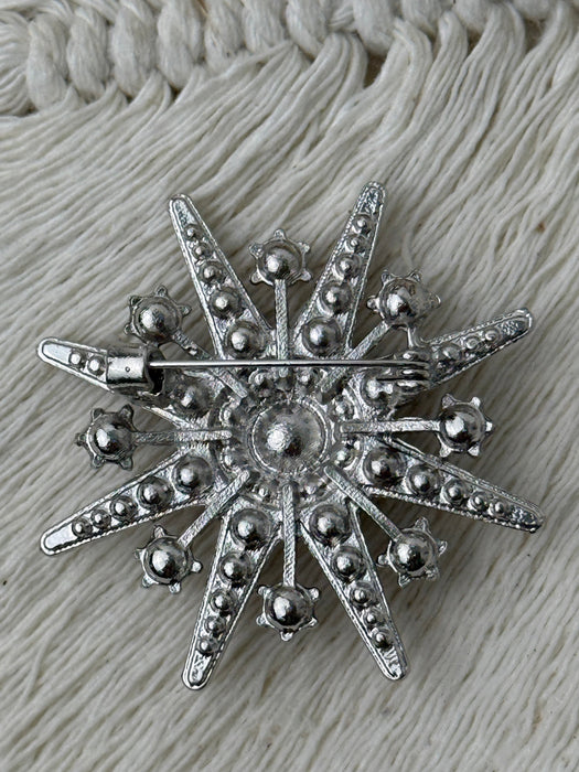back view of silver star-shaped brooch on a textured fabric background