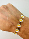 A gold-tone chain bracelet adorned with daisy flowers on a person's wrist.