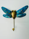 Handmade turquoise metal dragonfly hook with silver and gold accents on white background.
