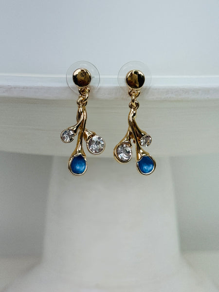 Gold-tone branch drop stud earrings with blue enamel teardrops and clear glass crystals on white background.