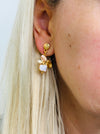 Gold-tone drop stud earrings with an enamel leaf cluster and bud-shaped charm in white, displayed on a model.