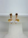 Gold-tone drop stud earrings with an enamel leaf cluster and bud-shaped charm in white, displayed on a white plate.