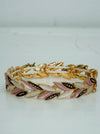 Gold-tone stretch bracelet with enamel leaf links in gold, rose gold and cream, displayed on a table.