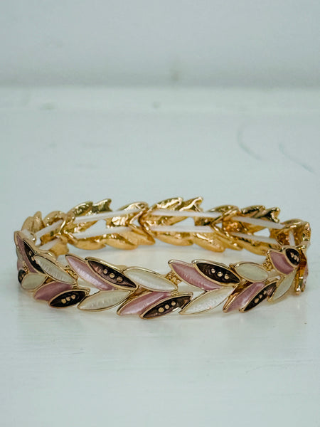 Gold-tone stretch bracelet with enamel leaf links in gold, rose gold and cream, displayed on a table.