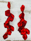 12 cm long statement drop earrings with cascading matte red acrylic petals and gold-tone metal accents, displayed on a table.