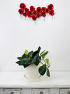 Metal poppy wall art displayed above a white shelf with plant décor