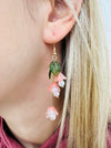 close-up of delicate bell flower drop earrings with soft peach petals and green leaf details.