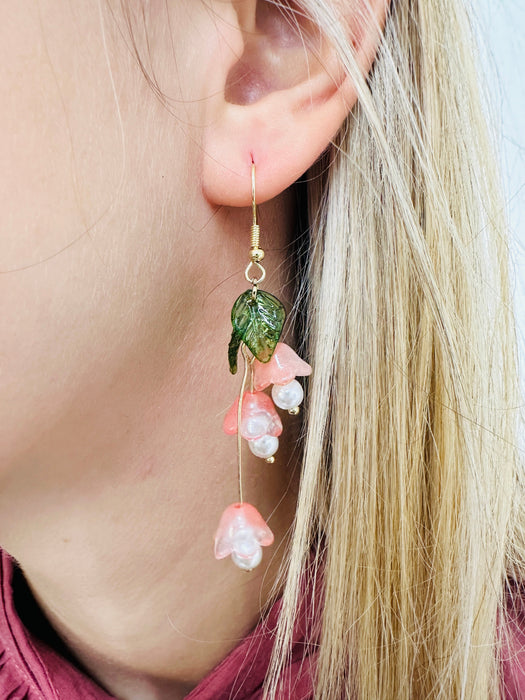 close-up of delicate bell flower drop earrings with soft peach petals and green leaf details.